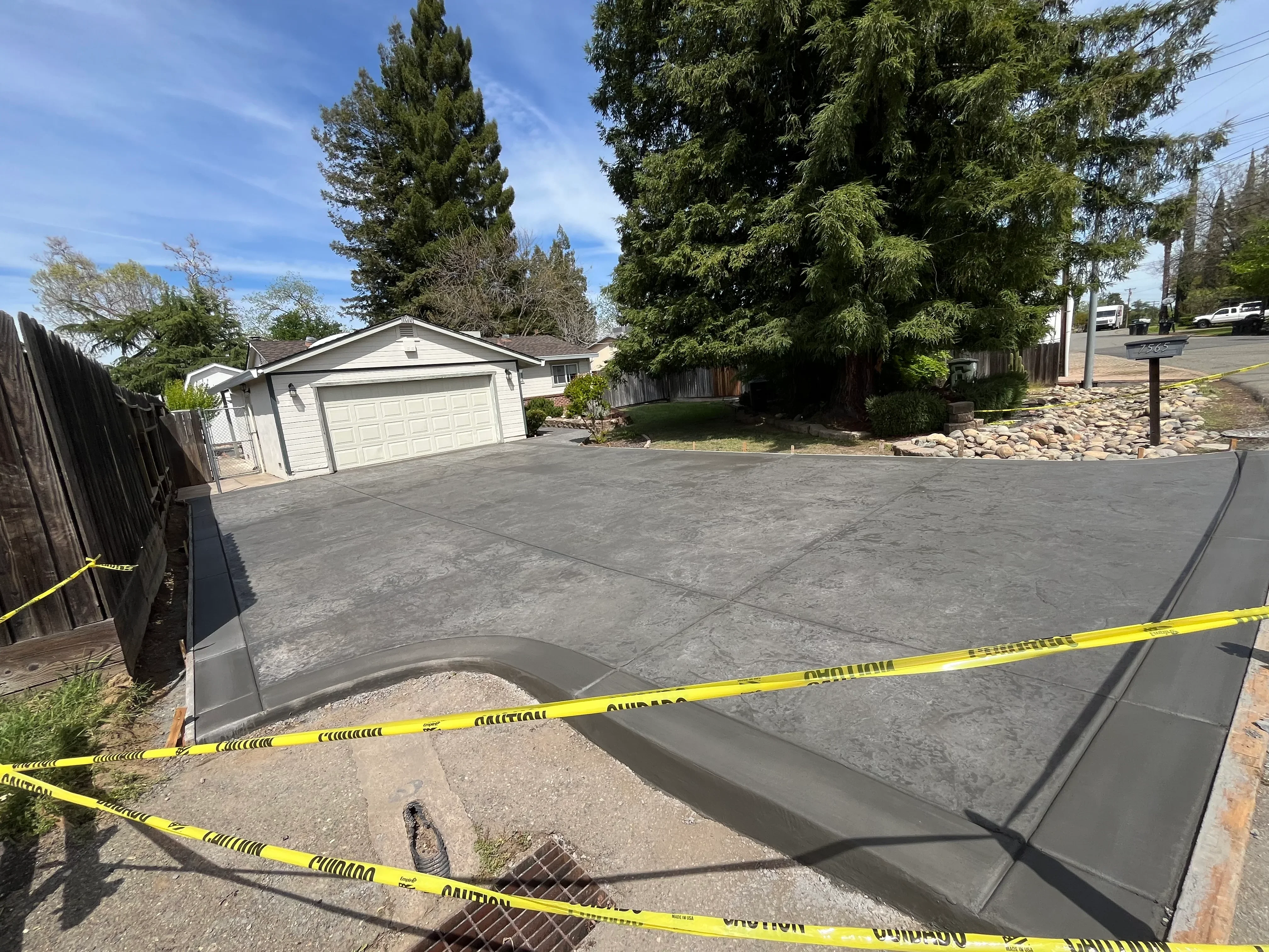 New concrete driveway with control joints during curing phase, residential home with garage in background