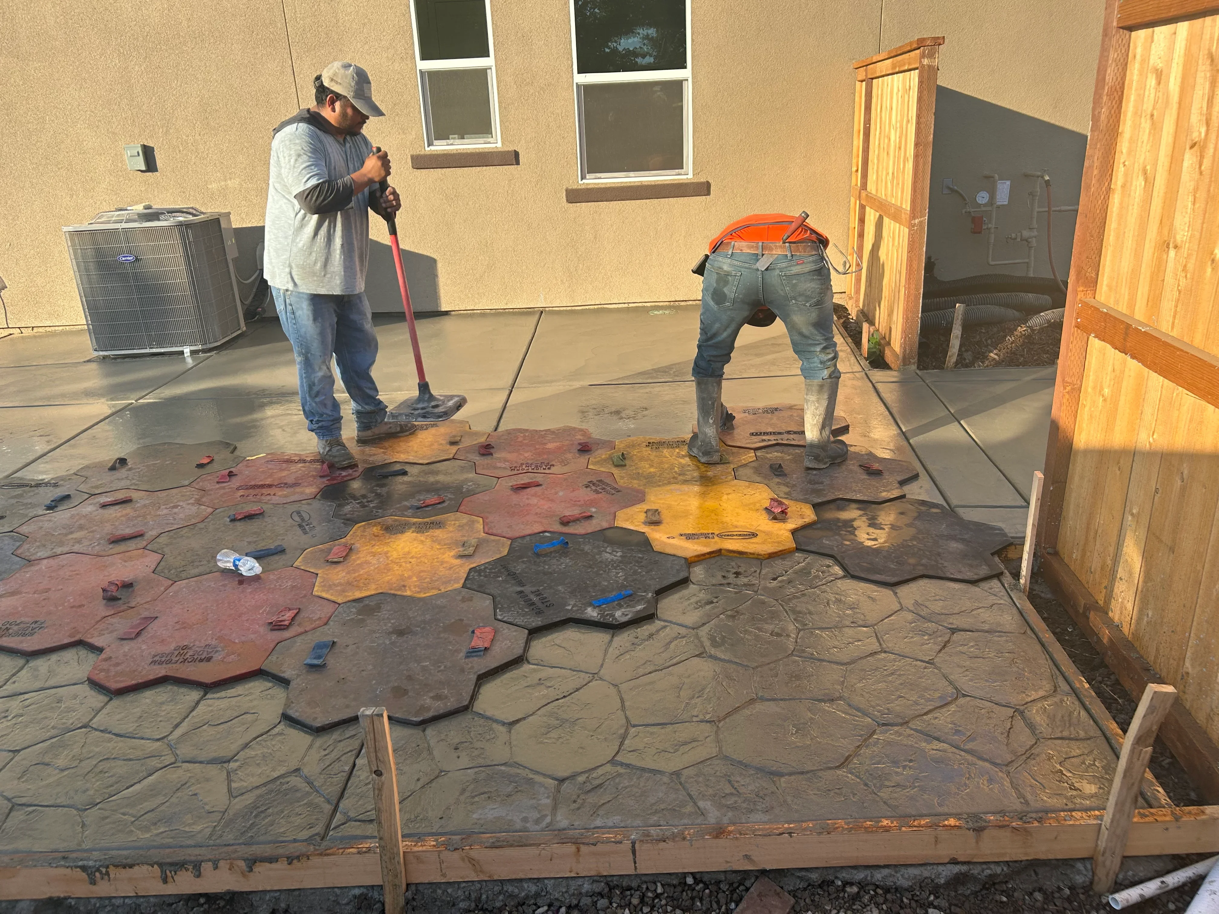 Workers installing decorative stamped concrete patio with multi-colored stone pattern design