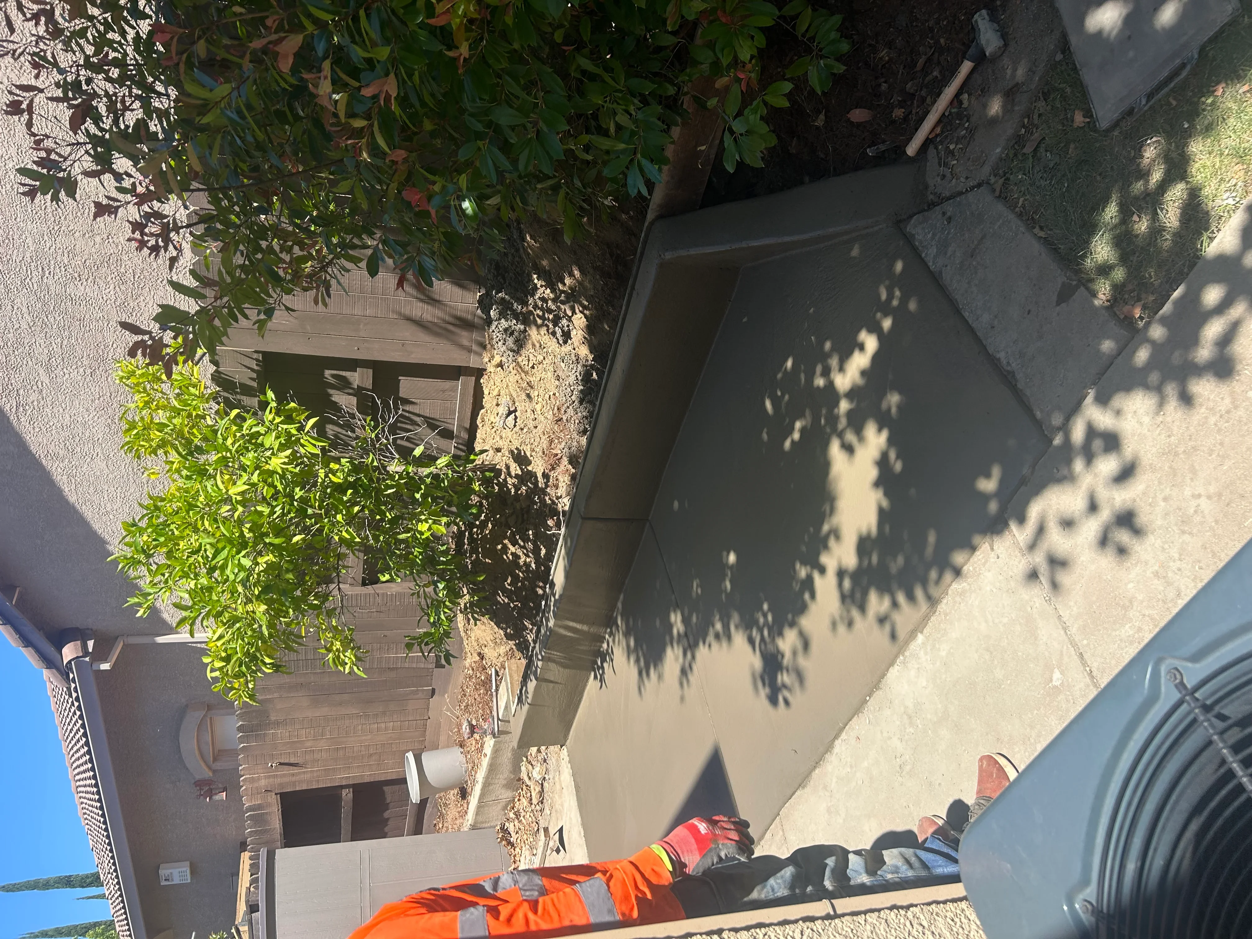 Worker in safety gear installing residential concrete patio with landscape plants nearby