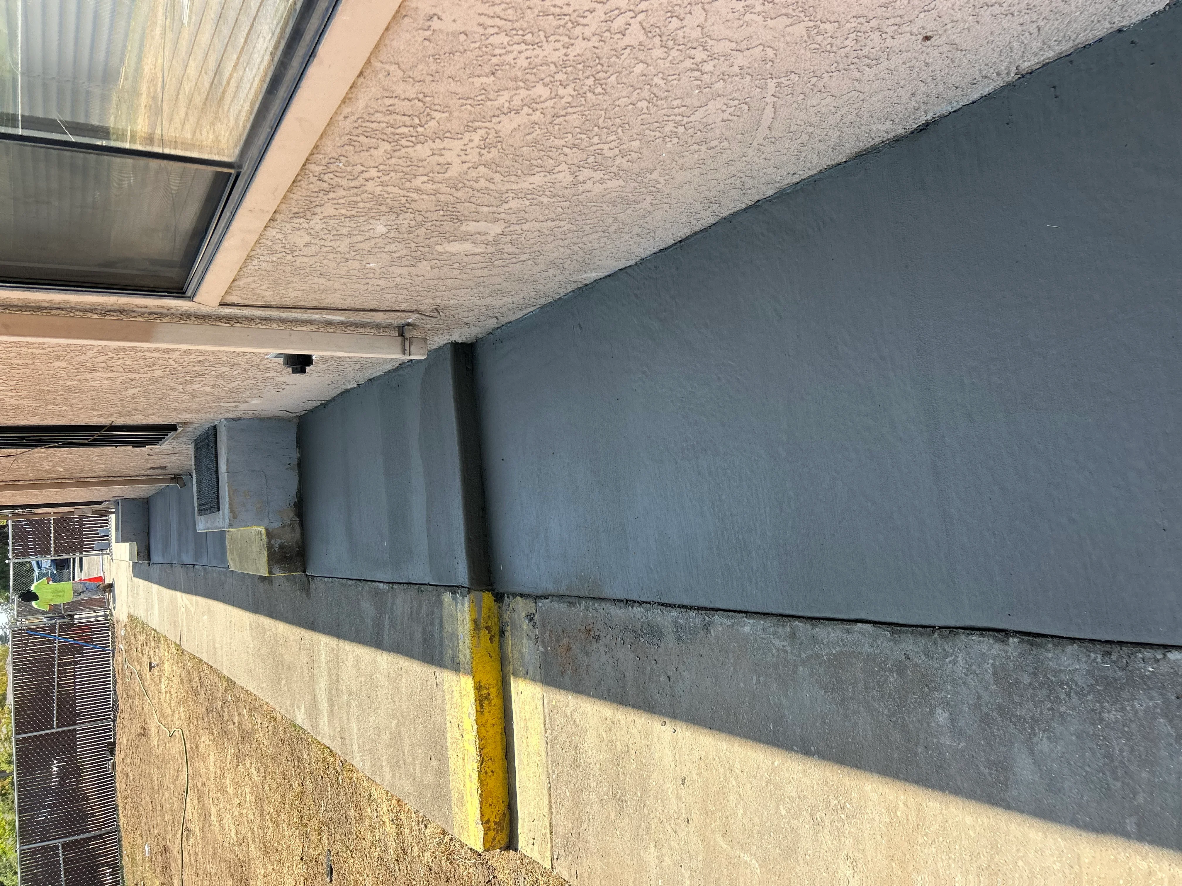 Concrete foundation wall with dark waterproofing membrane applied and yellow safety stripe marking