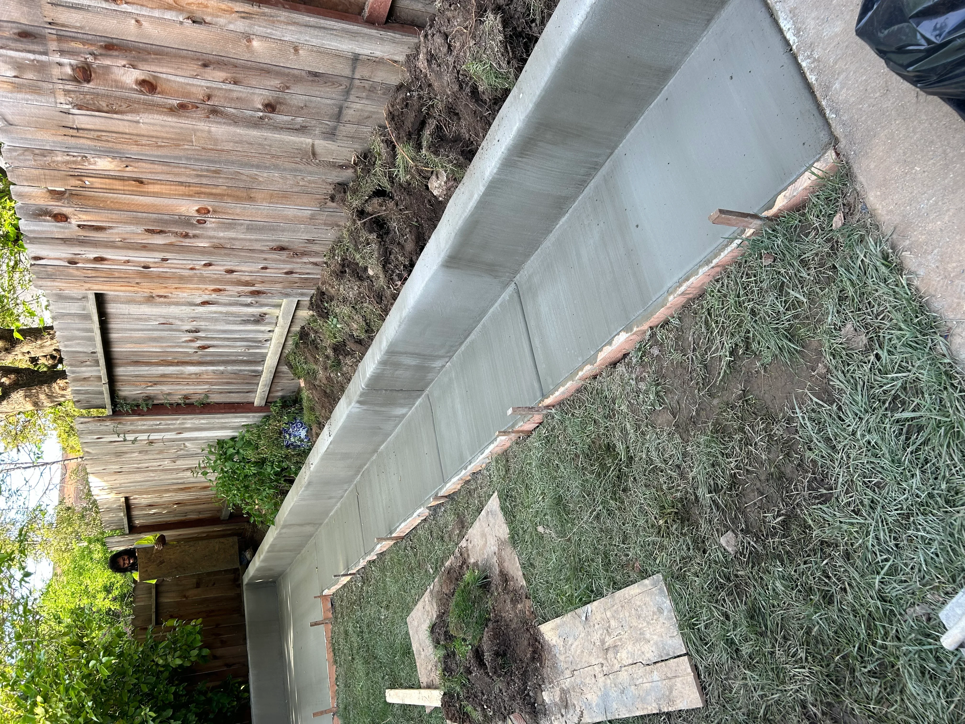 New concrete apron installation next to wooden building with brick foundation