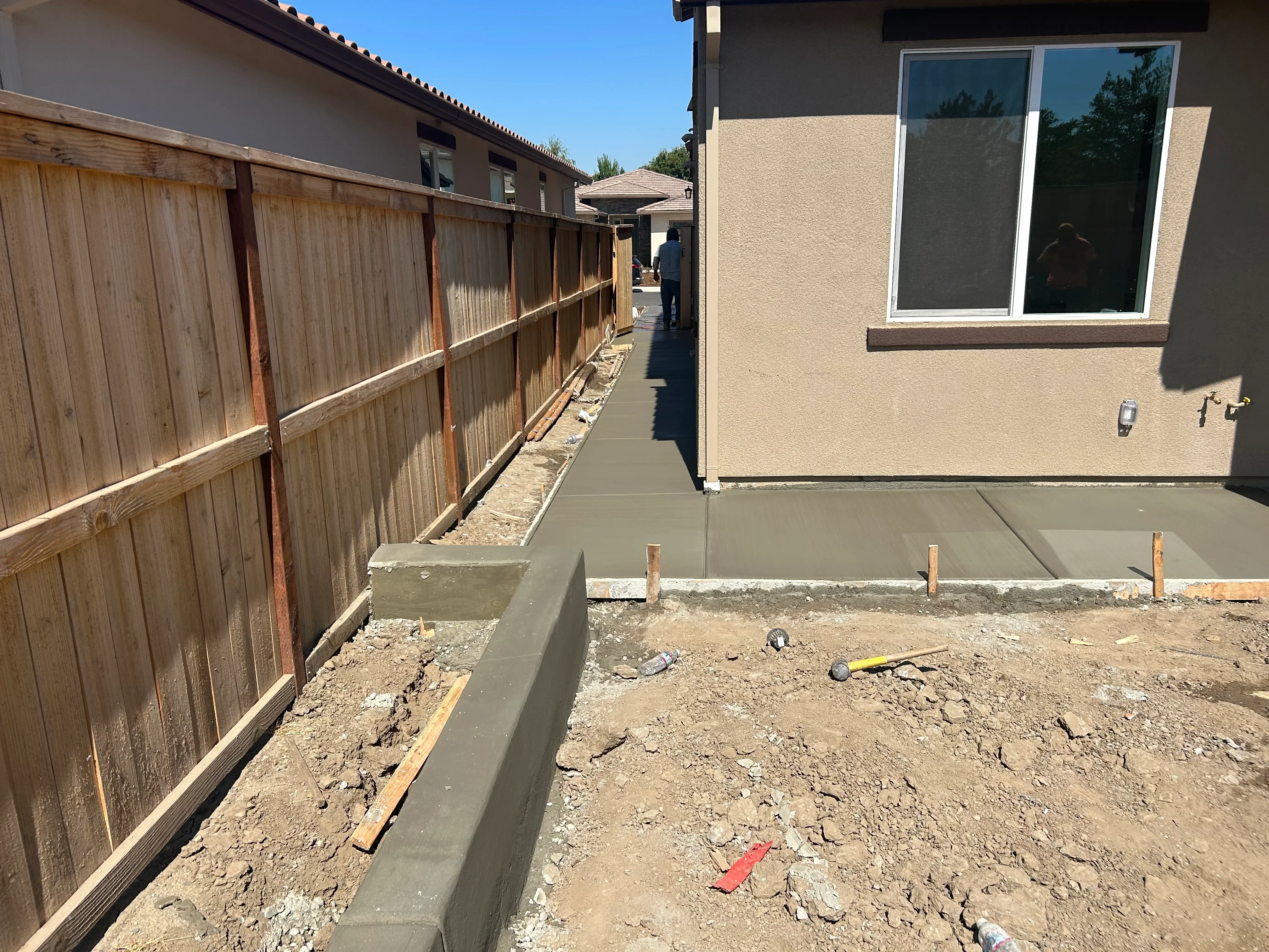 Newly poured concrete patio slab with control joints and wooden fence bordering residential property